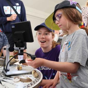 Young person and scientist look at microscope together they're both smiling