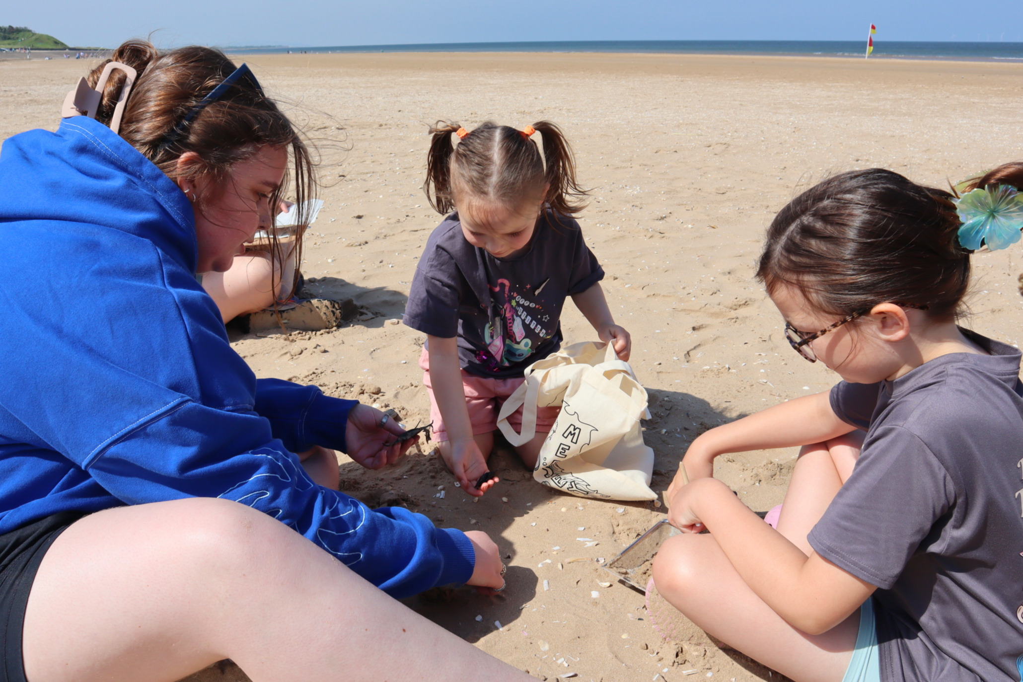 A woman and two children on the beach looking at marine wildlife